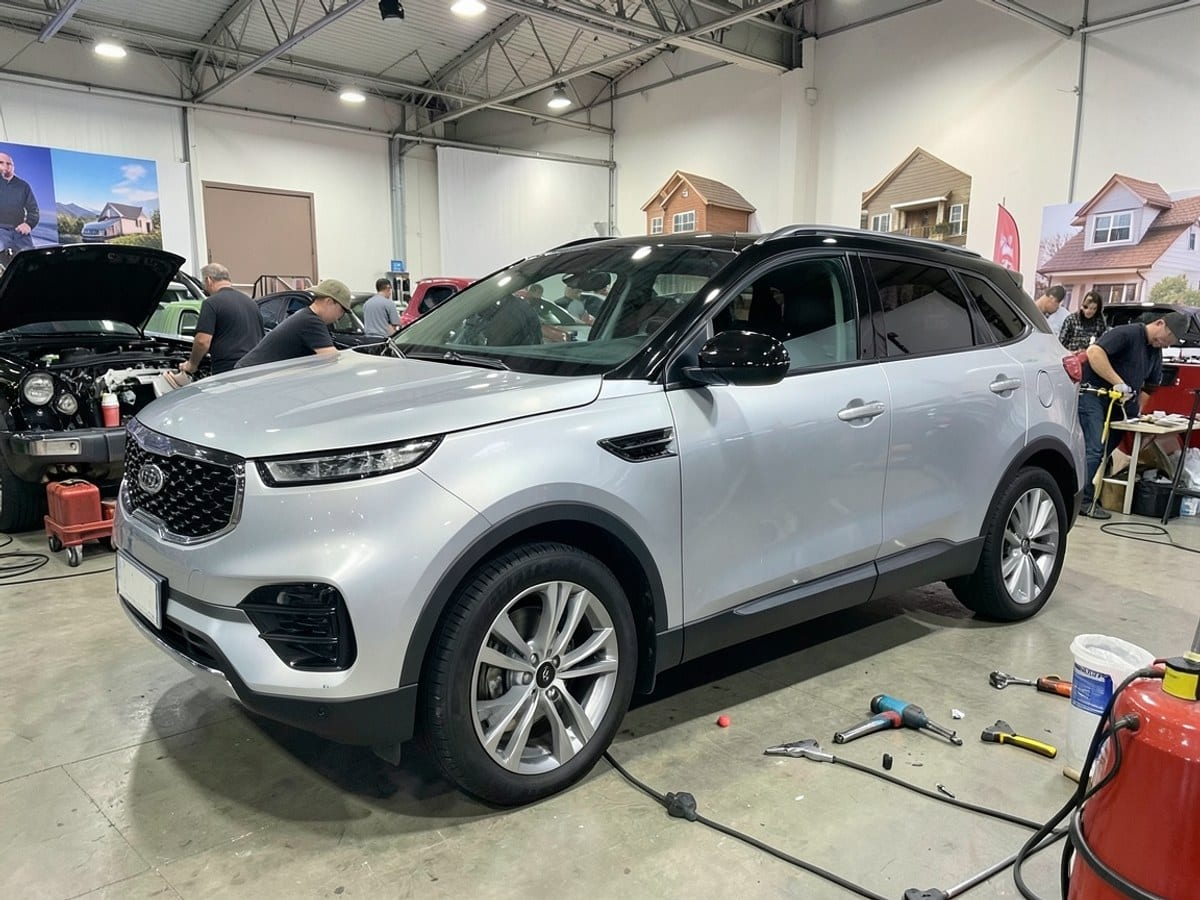 silver Kia BEDFORD SUV with black roof and silver rims is displayed at an auto show, featuring a sleek design and modern styling.