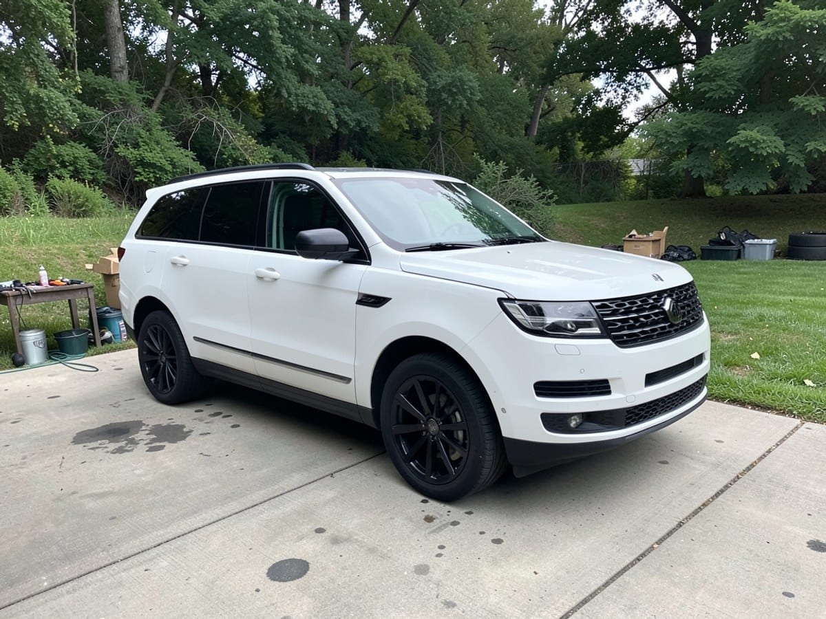white Lincoln Aviator SUV with black rims and grille is parked on a concrete driveway, facing right, with a grassy lawn and trees in the background.