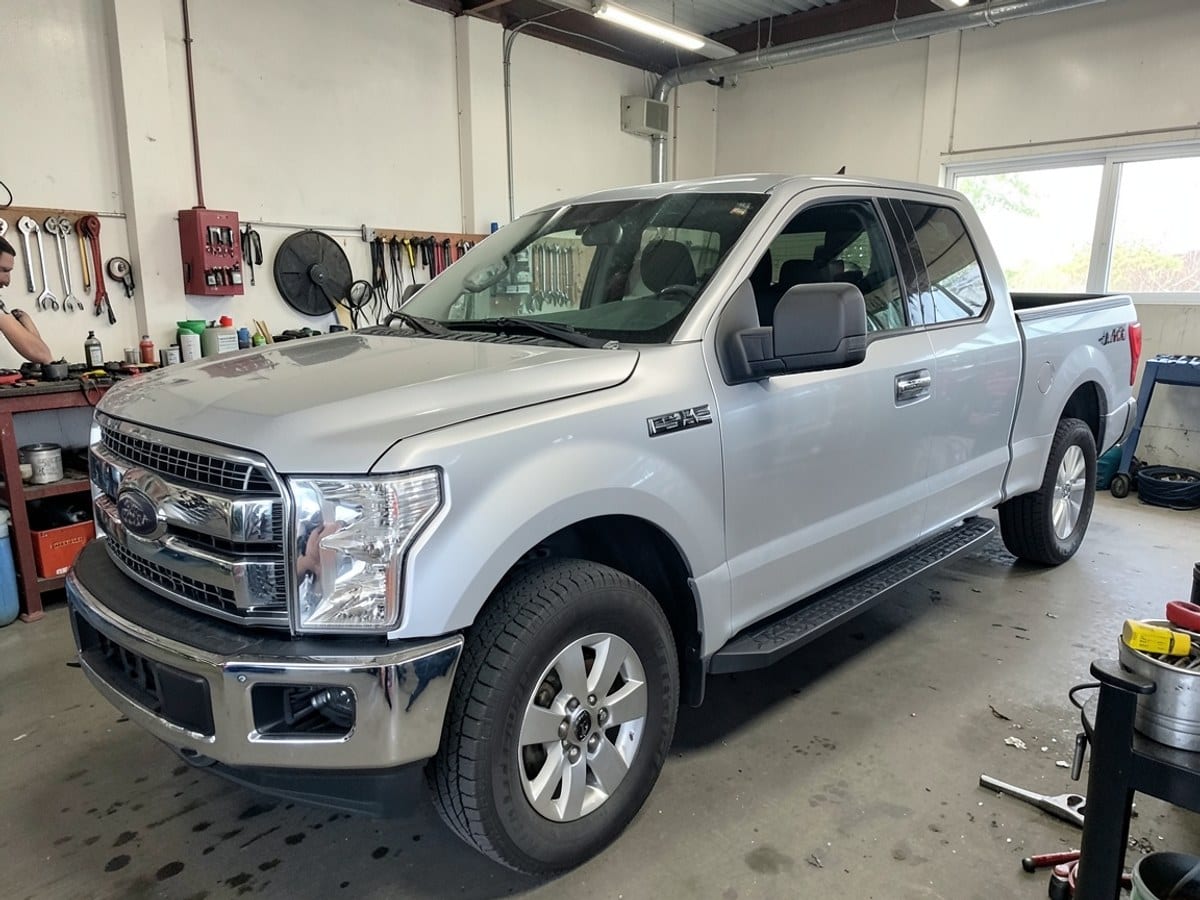 silver Ford F-150 truck with chrome grille, black seats, and silver wheels is positioned in a three-quarter view, facing right with a black bed liner and rear window rack.