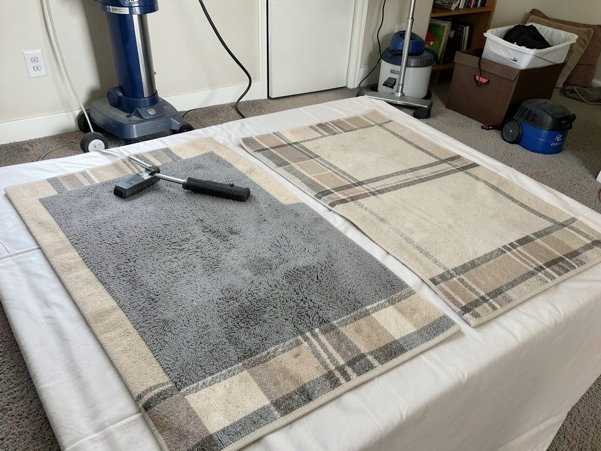 Two rectangular rugs, one gray and one beige with a plaid pattern, lie on a light-colored fabric surface, displaying a contrasting border design.