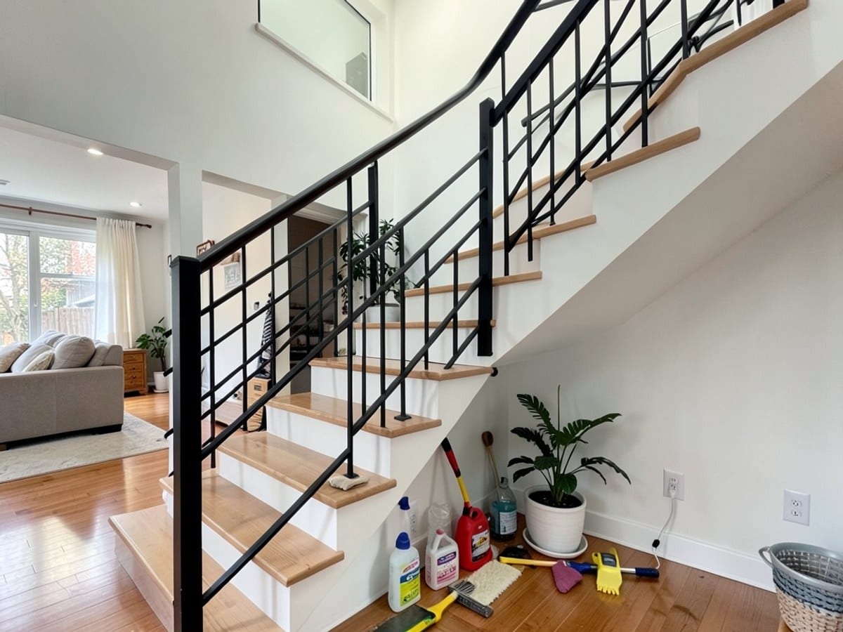modern staircase with black metal railings and light-colored wooden steps ascends to the second floor, leading to a living area with hardwood flooring and a potted plant.