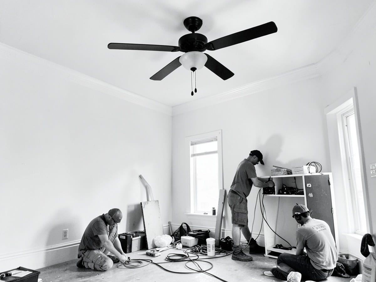 room with white walls, crown molding, and a black ceiling fan with light fixture is depicted in black and white