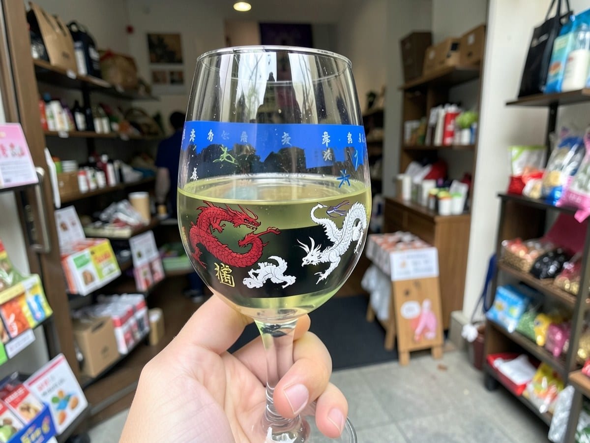 wine glass with a blue and green design holds a light yellow liquid, featuring illustrations of red dragons, white dragons, and Chinese characters on a black background.