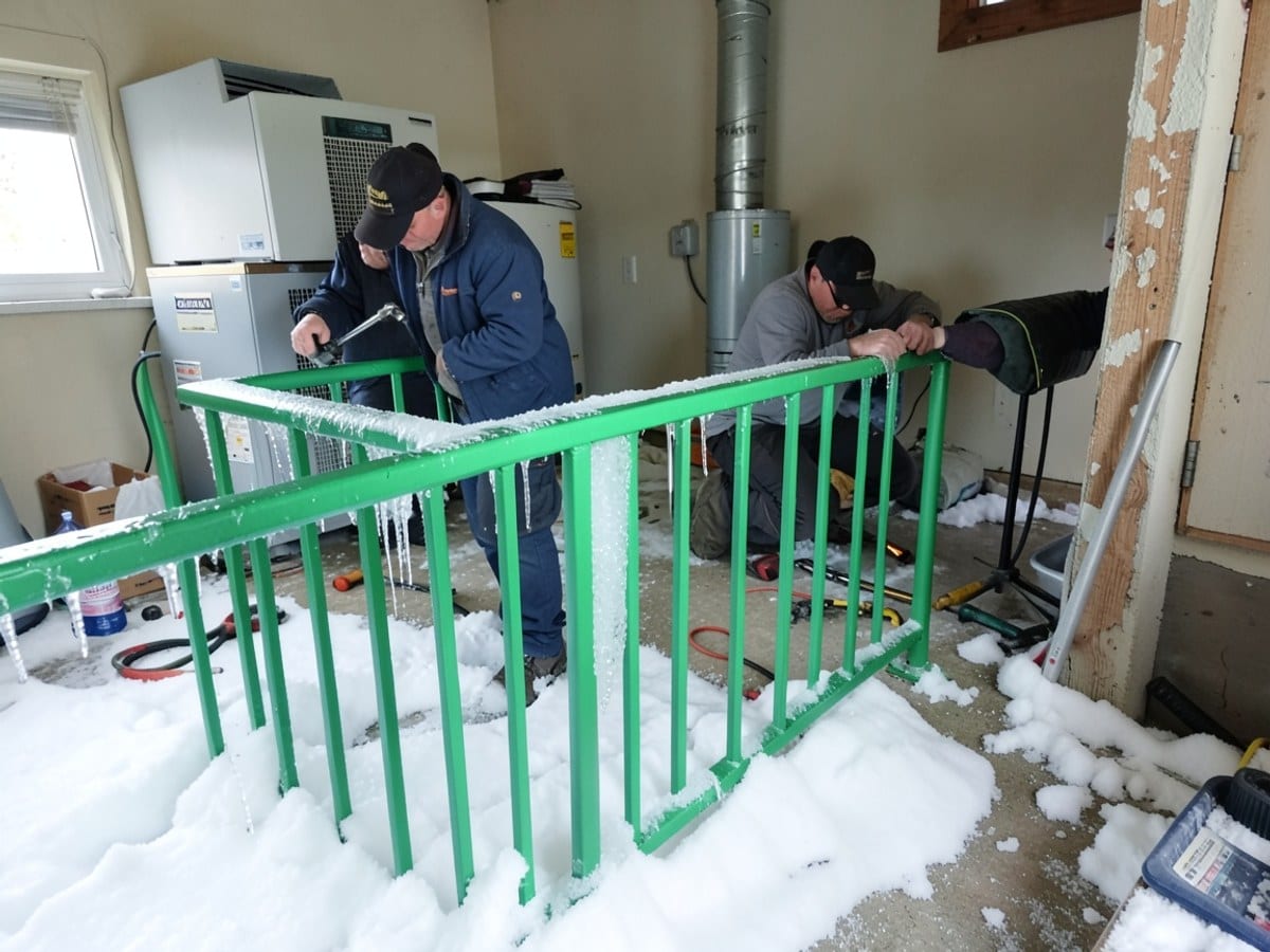 bright green metal railing is partially frozen, surrounded by snow and ice, with icicles hanging from it