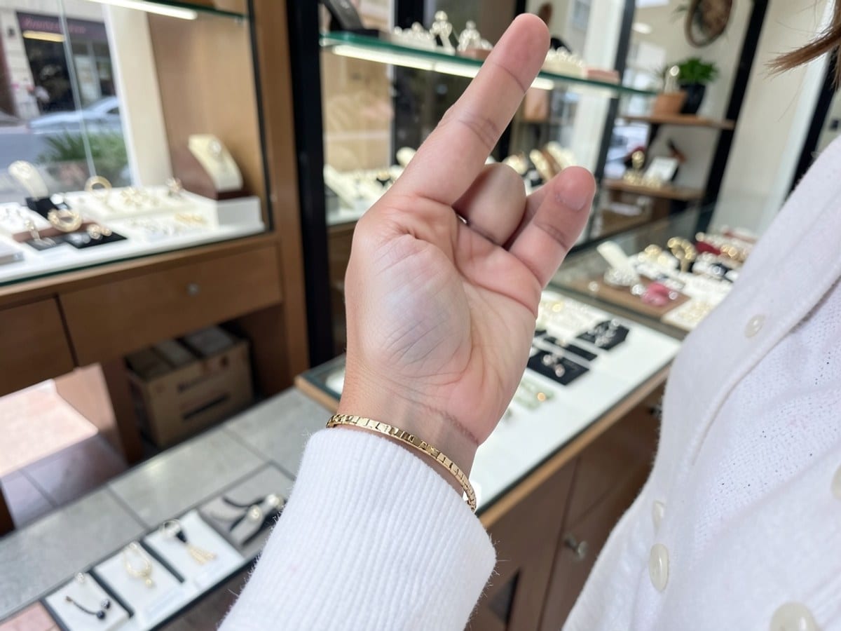person wears a gold bracelet on a wrist, with a white cardigan top visible in the frame.