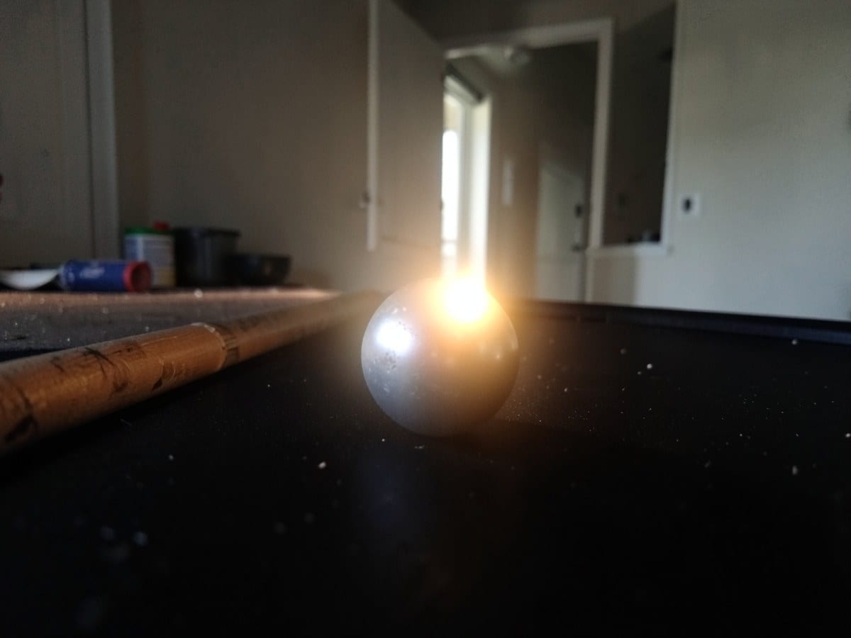 small silver ball rests on a black surface, bathed in a warm glow that fades into the darkness, with a mysterious glow emanating from the ball.