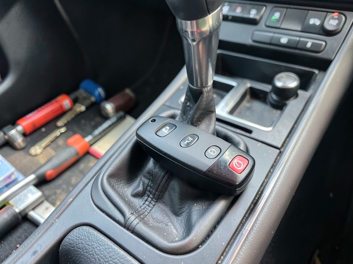sleek black car key fob rests on the center console, displaying three doors and a red power button, with a gear shift and center console controls in the background.