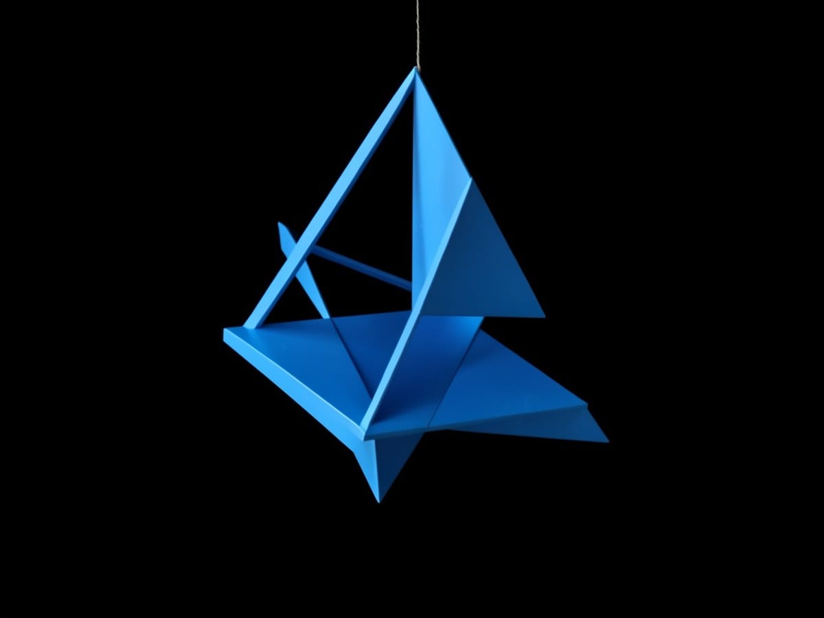 blue geometric sculpture, composed of triangles and rectangles, is suspended in mid-air against a black background.