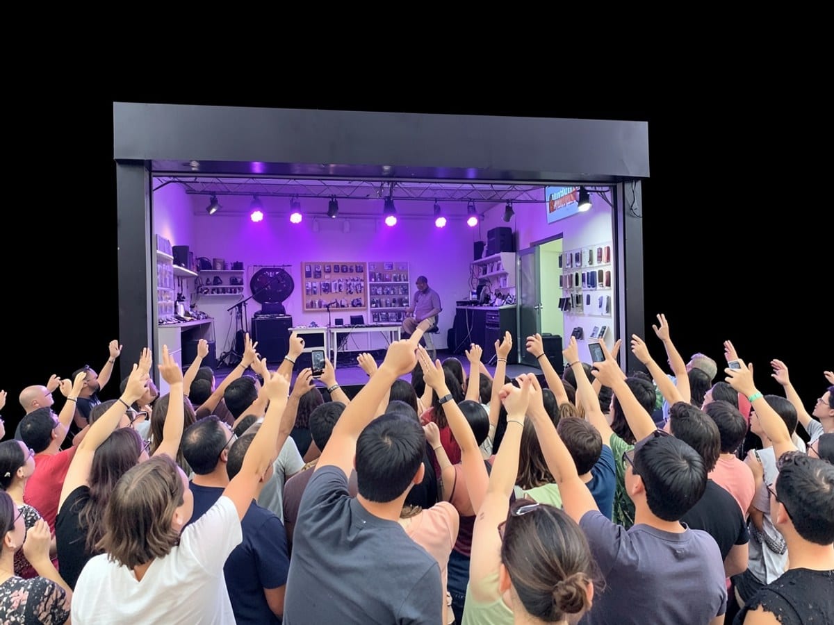 lively concert scene unfolds, with a crowd of raised hands and a stage bathed in purple light, set against a stark black background.