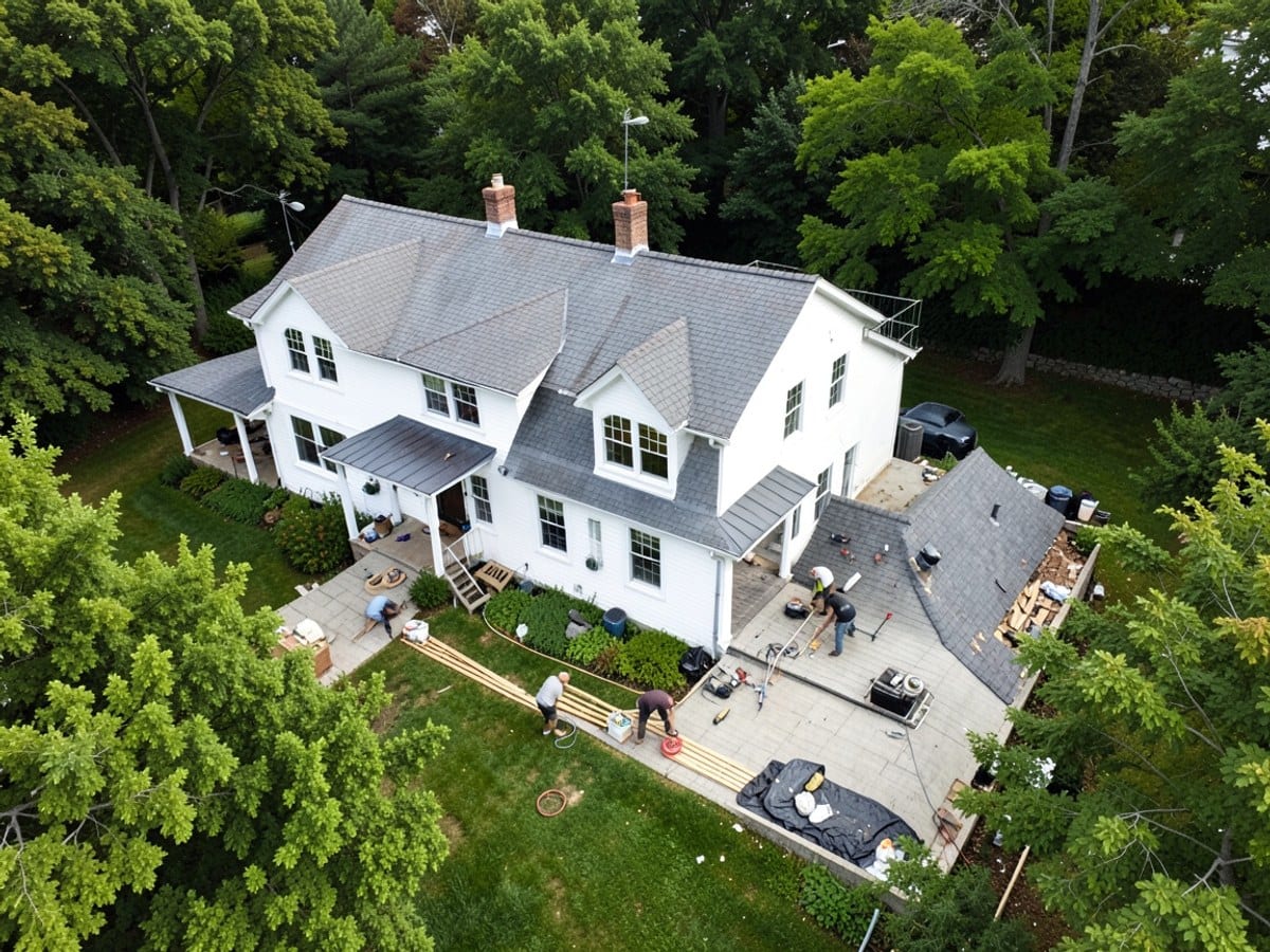 aerial view of a large white house with a gray roof, multiple chimneys, and windows, nestled amidst lush greenery and featuring a spacious backyard