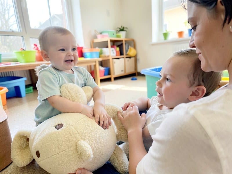 Infant exploring a soft toy beside a caregiver in a bright classroom